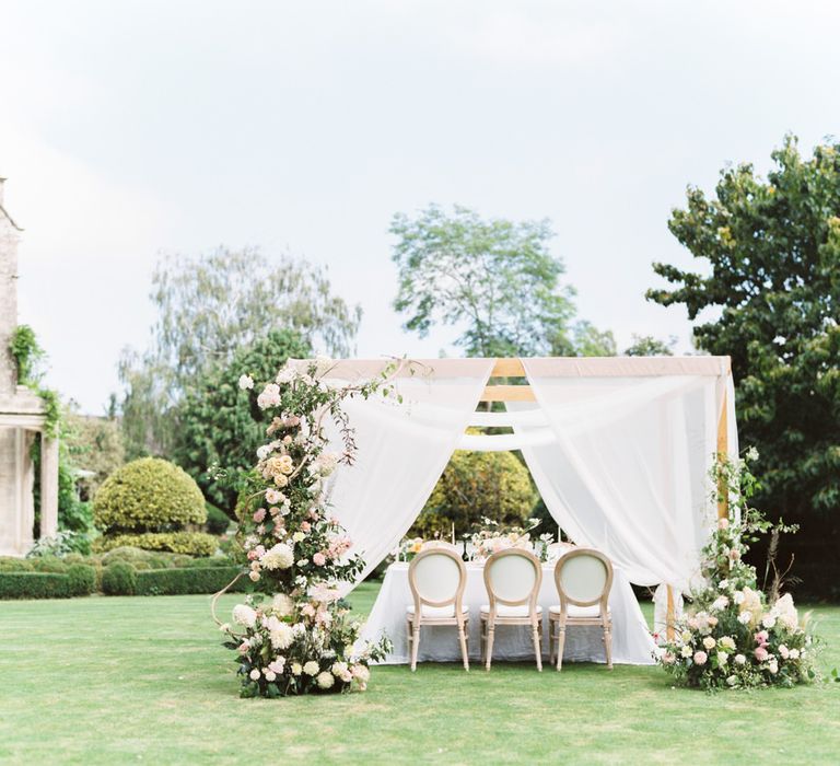 White fabric pergola decorated with flower garlands and centrepieces for English garden party wedding