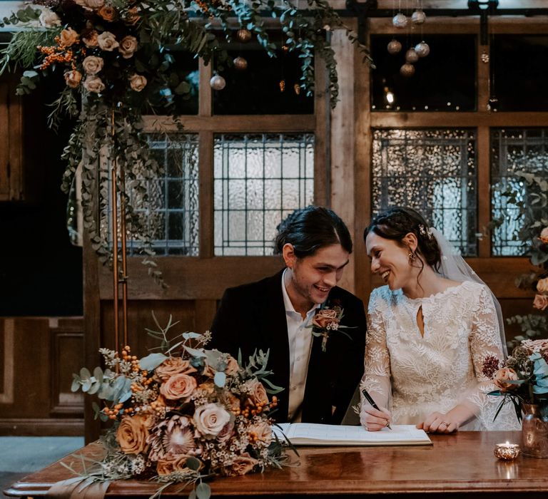 Bride and groom signing wedding certificate framed by stunning floral with peach roses