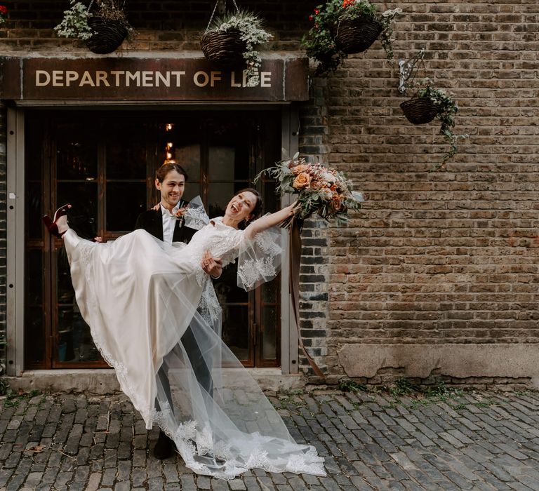 Groom holding his new wife with her leg up in the air showing her stunning silk and lace wedding dress