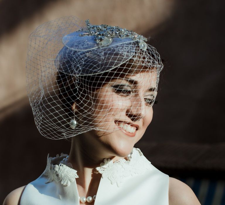 Bride wearing a vintage style wedding dress with a lace collar, and bridal fascinator with white netting