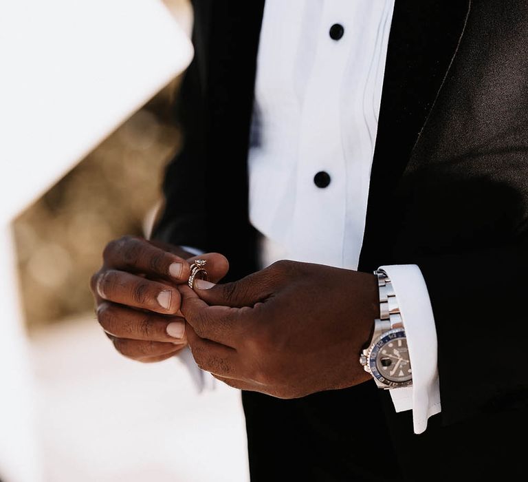 Groom in a tuxedo holding the diamond wedding ring