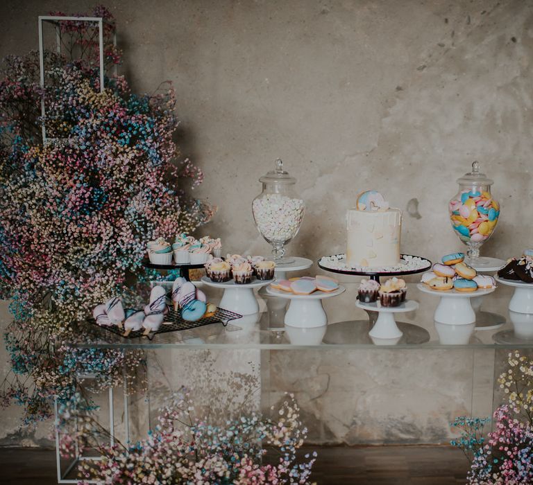 Candy crush inspired dessert table with gypsophila flower clouds that look like rainbow drops, flying saucers, doughnuts, cupcakes, macaroons and a drip wedding cake 