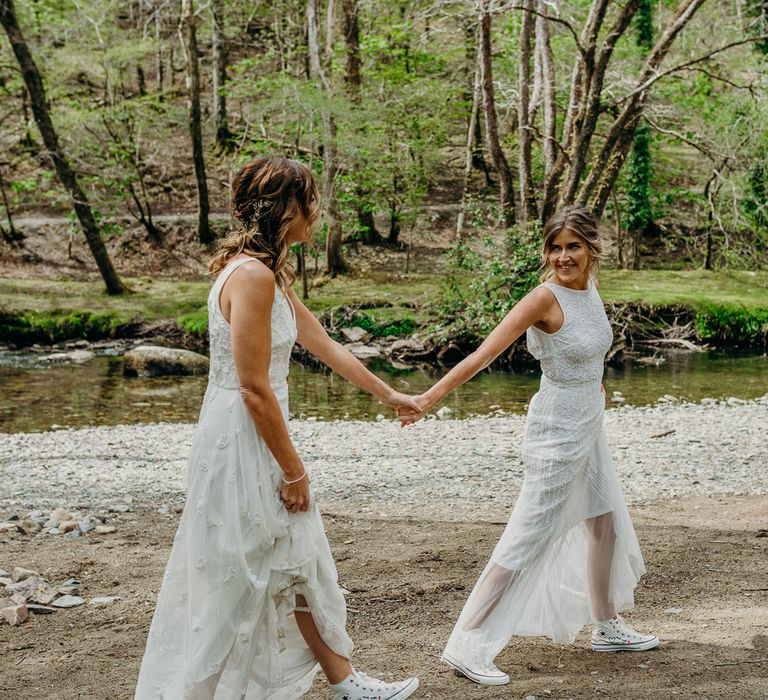 Bride leads wife through woodlands on their wedding day whilst wearing boho chic wedding gowns