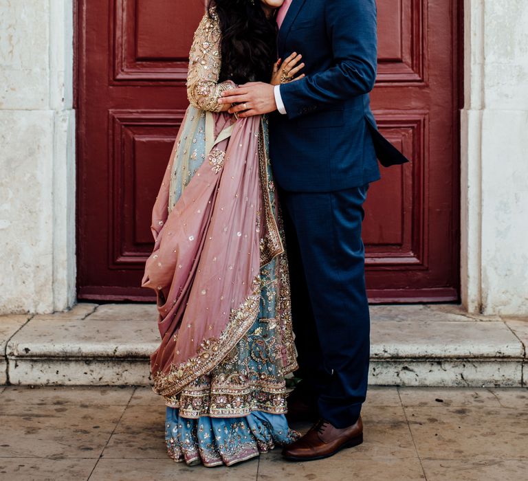 Bride rests her head on grooms chest as she wears brightly coloured saree 