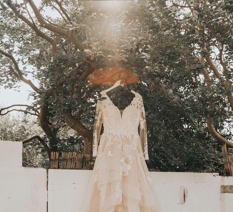 A wedding dress with large layered tulle skirt hangs from a tree.