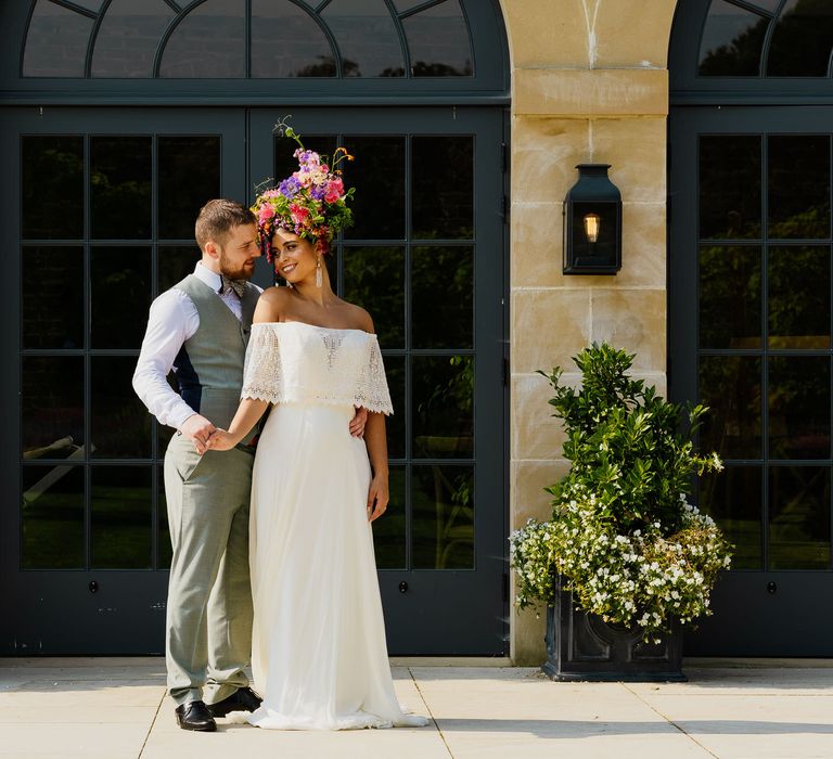 Bride in a strapless wedding dress with lace layer wearing a colourful wildflower crown standing outside The Fig House at Middleton Lodge 