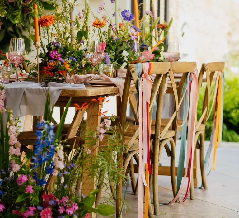 Fiesta theme wedding table decor with ribbon chair backs, wildflower centrepieces, taper candles and coloured glassware 