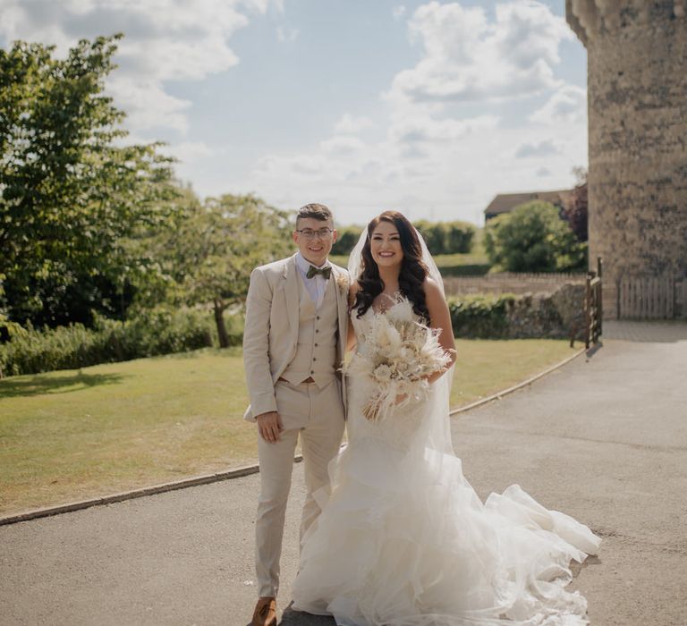 Portrait of the Bride in a Mori Lee wedding dress and the groom in a beige suit outside their Cooling Castle Barn wedding venue 