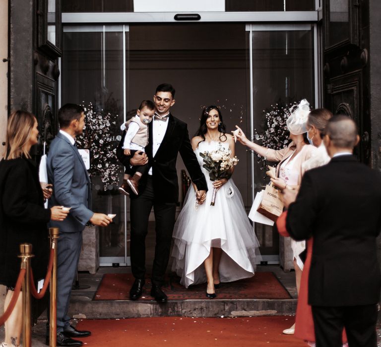 Bride & groom leaving wedding ceremony into confetti thrown by wedding party 