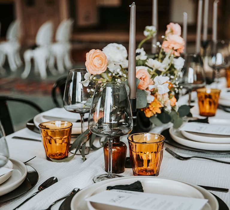 Place setting with black charger plate and white table wear, pewter cutler and orange coloured glassware 