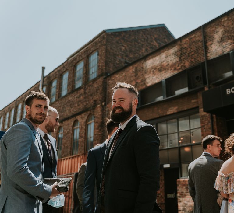 Groom stands outside the Boiler Shop with wedding party as the sun shines