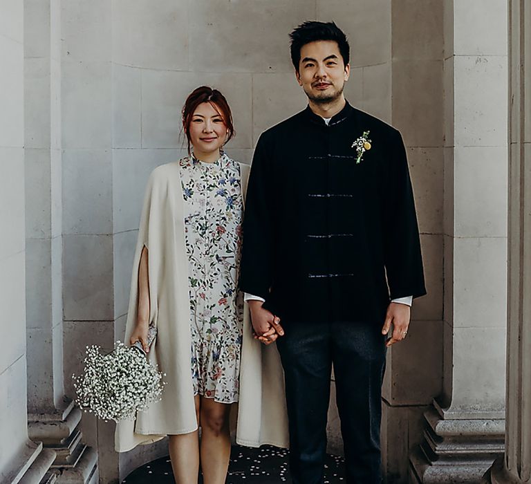 Bride and groom portrait at Old Marylebone Town Hall with East Asian groom in a blue velvet jacket and bride in a floral wedding dress and beige cape coat 