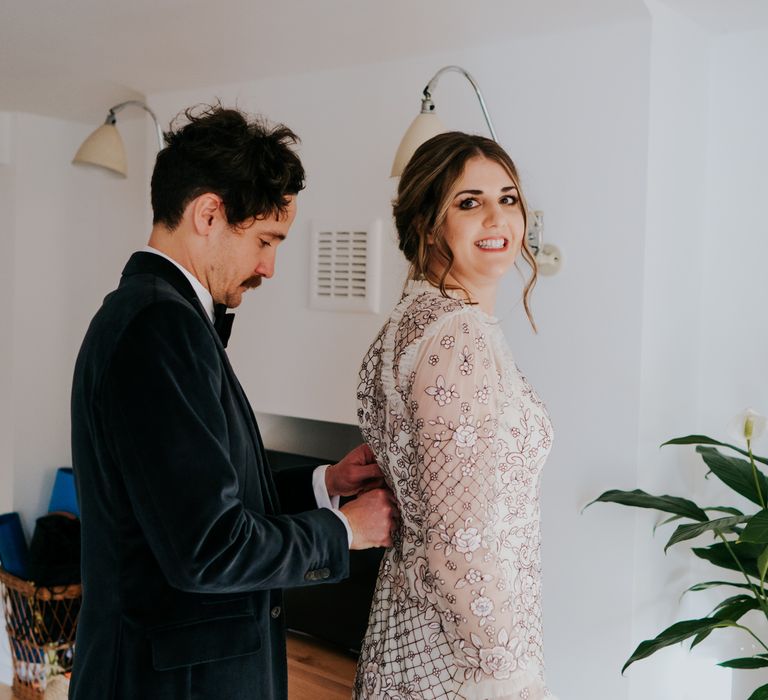 Bride has her Needle And Thread wedding dress done up by groom on their wedding day