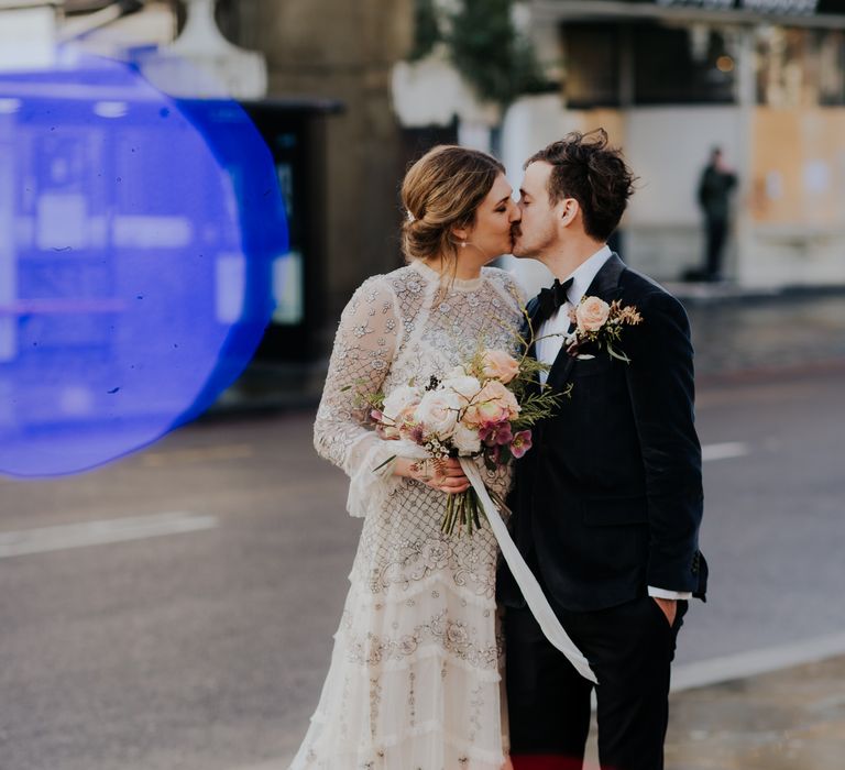 Bride & groom kiss outdoors as they walk through the streets with one another