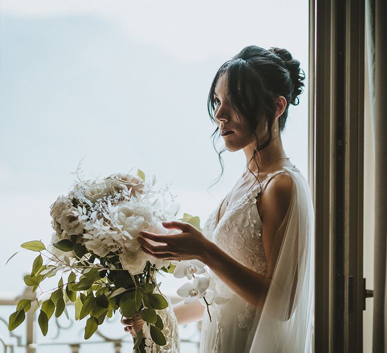 Bride looks out bright window before wedding ceremony