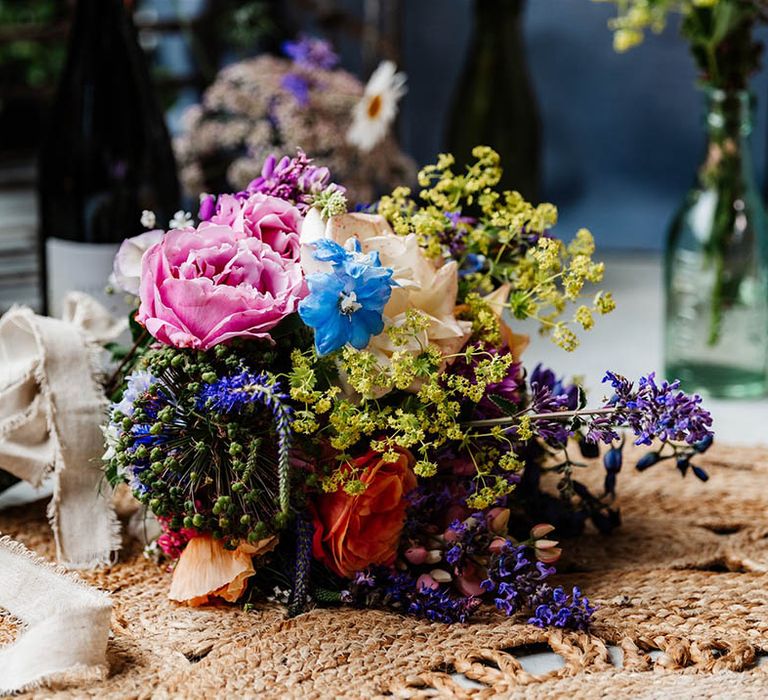 Colourful wildflower wedding bouquet resting on a wicker rug 