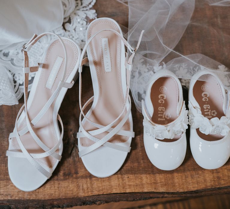 White strapped heeled sandals next to chide white sandals with strap next to wedding dress and veil at Tythe Barn wedding with barn wedding flowers