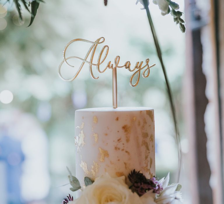 White wedding cake with gold leaf details, white rose decor and cake topper reading 'Always' at Tythe Barn wedding with barn wedding flowers