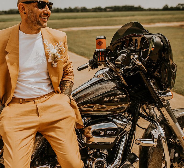 Stylish groom in a coloured mustard suit sitting on his Harley Davidson motorcycle 