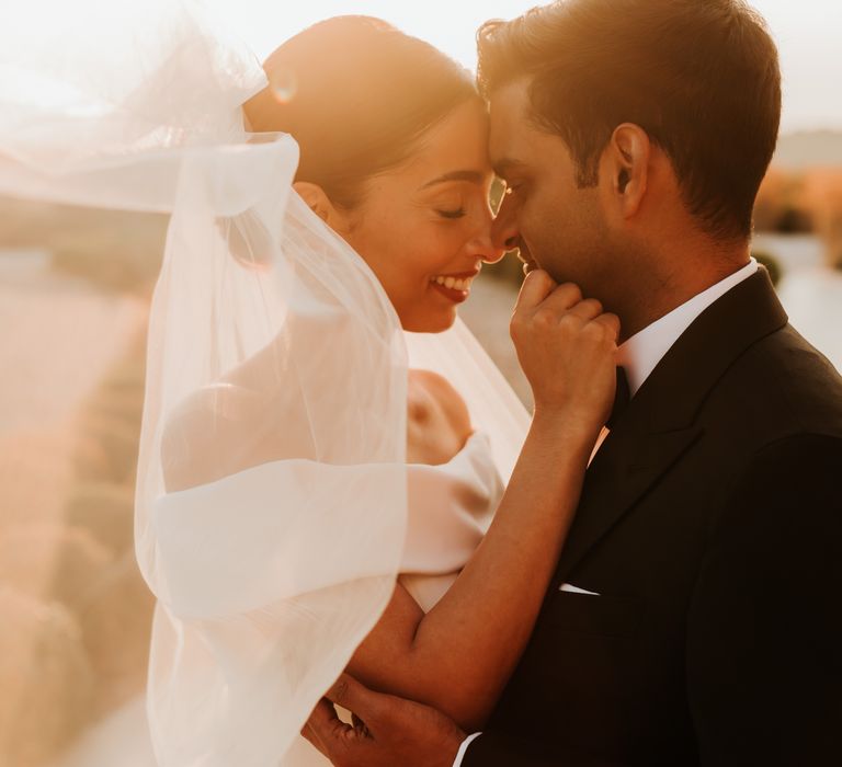 Bride & groom kiss during sunset as brides veil blows around them in the wind | Hannah MacGregor Photo & Film