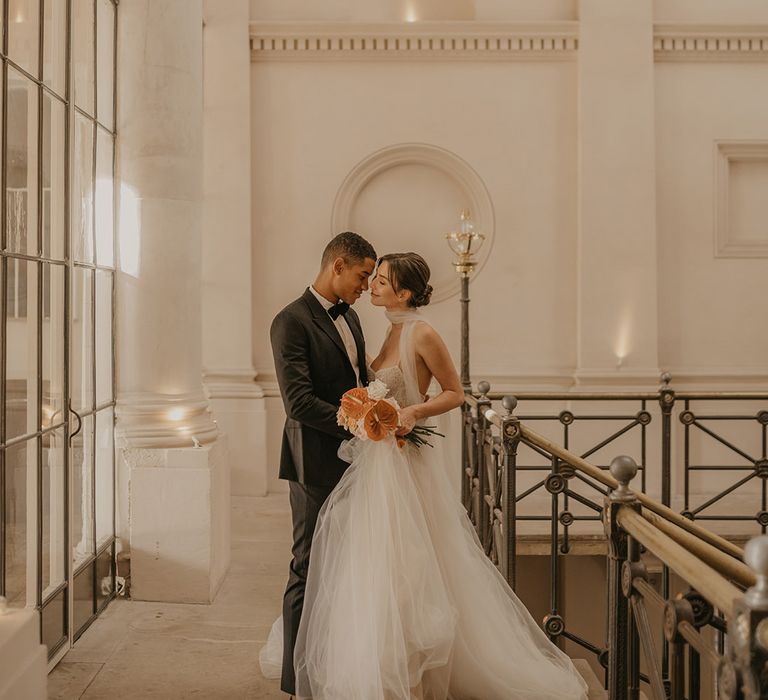 Bride in a tulle skirt wedding dress with sequin bodice standing on the stairs at Clerkenwell House with her groom in a tuxedo 