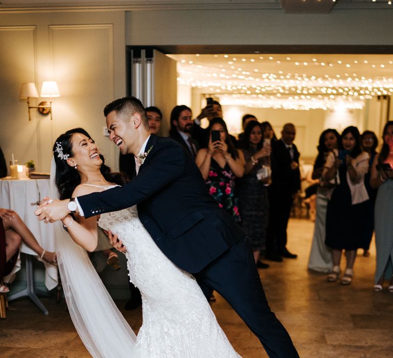 First dance with groom in a navy suit leaning his bride over in a lace embellished wedding dress