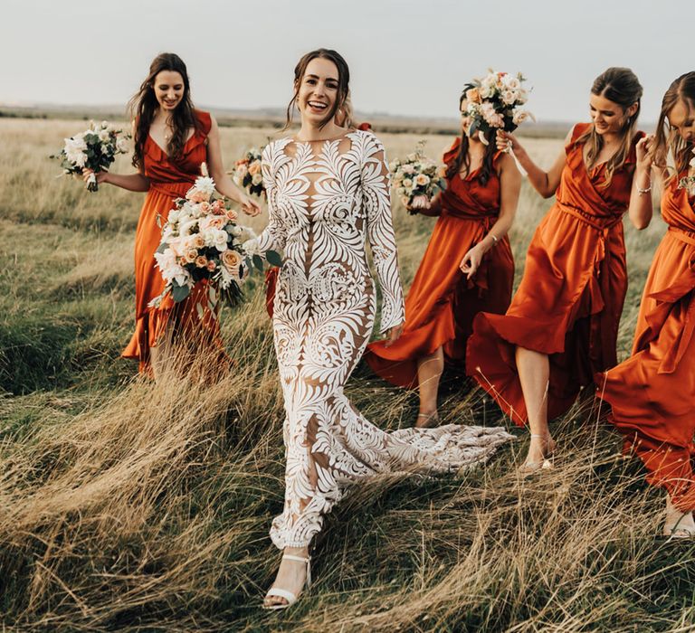 Bride in long lace boho wedding dress smiles with bride maids in Satin bridesmaid dresses in open natural setting