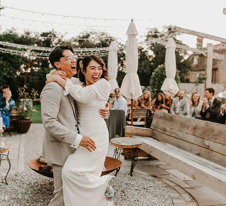 Bride & groom embrace outdoors as wedding guests watch 