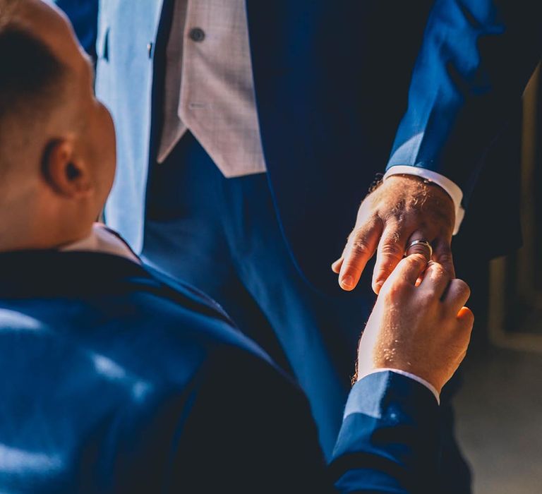 Blue wedding suits for grooms as they exchange wedding rings