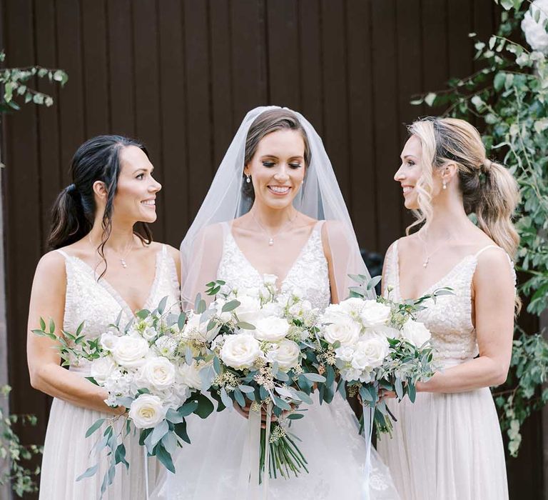 Bridal party portrait with bridesmaids in white dresses, and the bride in a Martina Liana wedding dress holding white rose and eucalyptus bouquets 