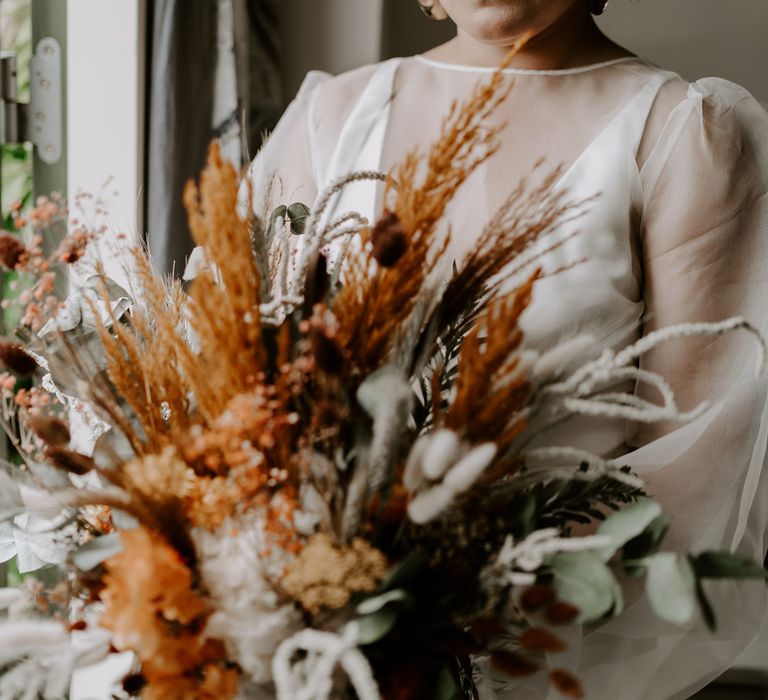 Bride on the wedding morning holding a orange and green dried flower wedding bouquet 