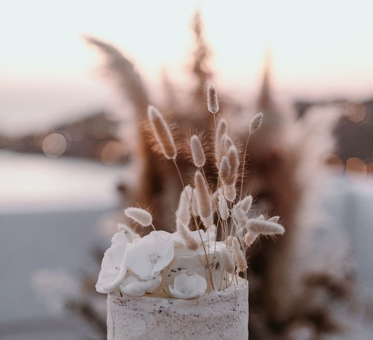 Three tier rustic wedding cake complete with white frosting and pampas grass decor