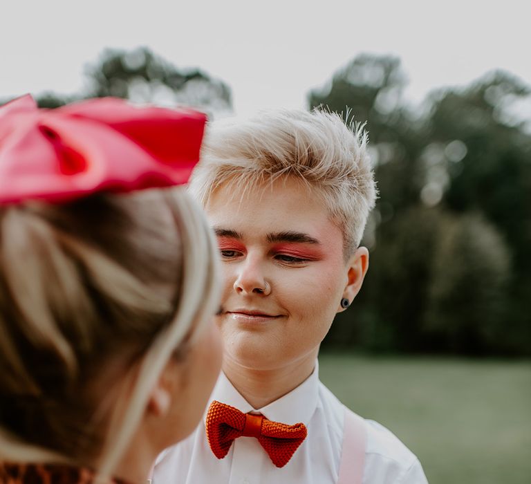 LGBTQI+ wedding with bride with short hair wearing braces and bow tie with red eyeshadow makeup 