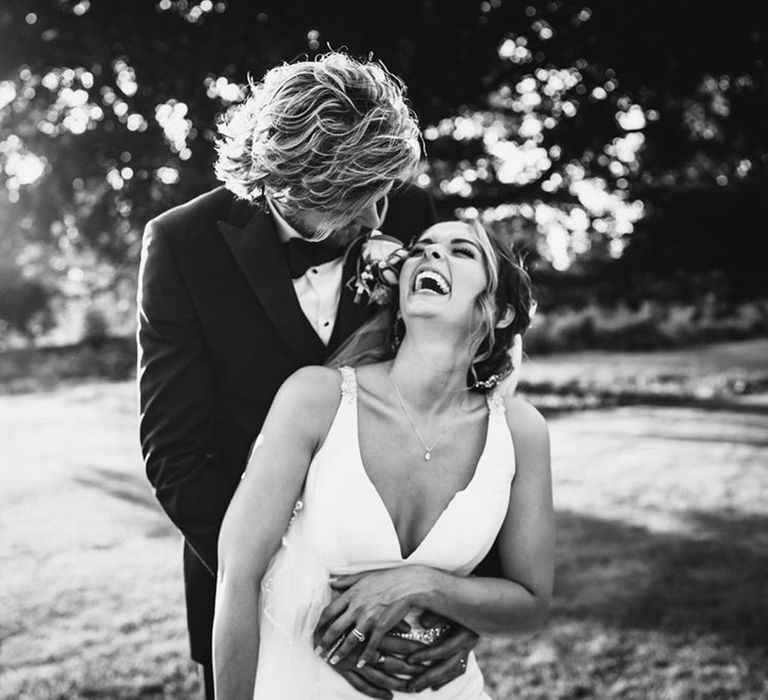 Couple laughing in black tuxedo and V neck fishtail wedding dress at Elmore Court