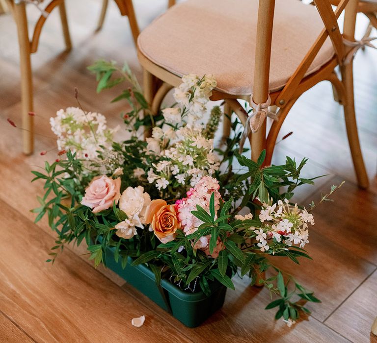 Potted plant aisle decoration with pink, white and orange flowers and light wooden seats with a pink base