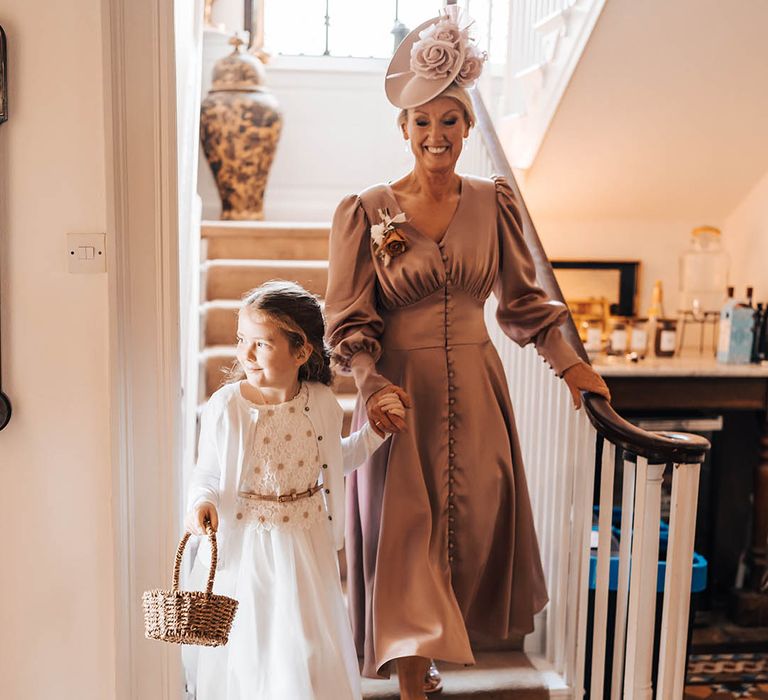 Flower girl in white dress with daisy top holding wicker basket and guest in brown dress with bishop sleeves