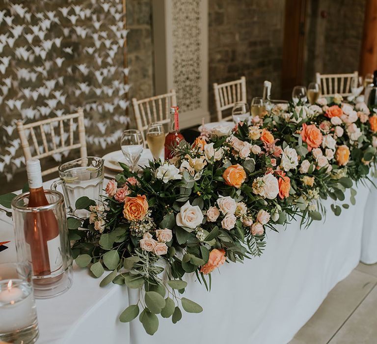 Top table wedding decor with bright orange and pink rose wedding flower display and DIY paper crane backdrop