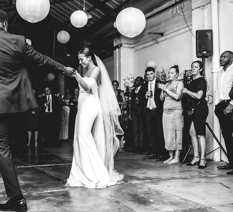 Groom in black tie pulls the bride out onto the dance floor for their first dance