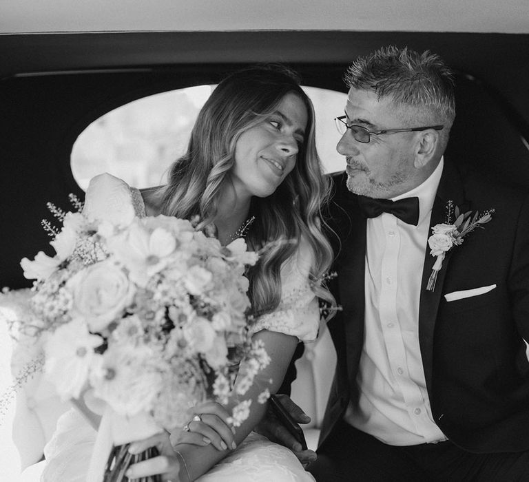 Bride in puff sleeve wedding dress looks lovingly at father as they sit in the wedding car on the way to the wedding 