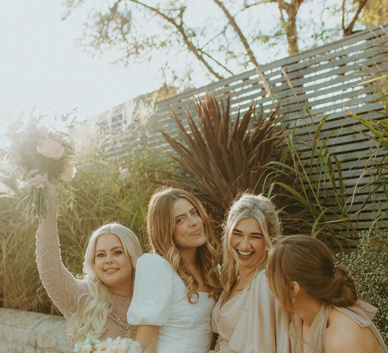 Bride in puff sleeve wedding dress smiles with bridesmaids in champagne gold dresses in different styles