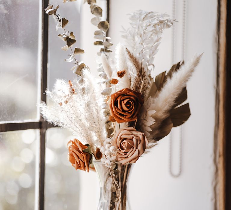 Rust and toffee roses with dried grass in glass vase for wedding decor 