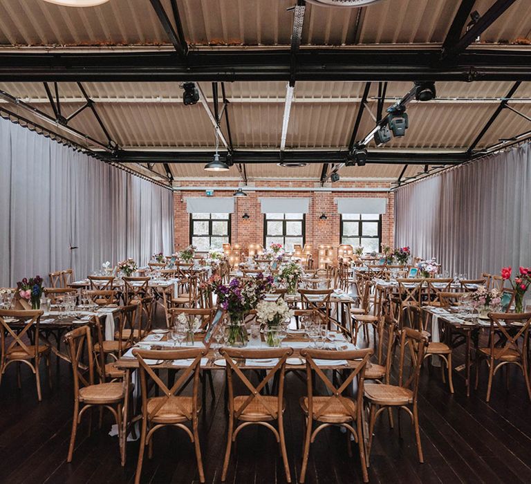 Wooden tables with white table runners and lots of bright spring flowers at industrial wedding venue, Bowers Mill 