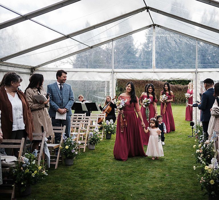 Bridesmaids in wine bridesmaid dresses walk down the aisle for outdoor wedding in marquee 