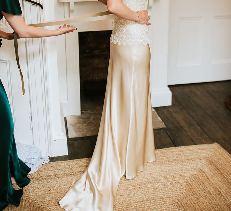 Bride wears gold silk wedding dress complete with delicate lace overlay as bridesmaid ties ribbon to the back 