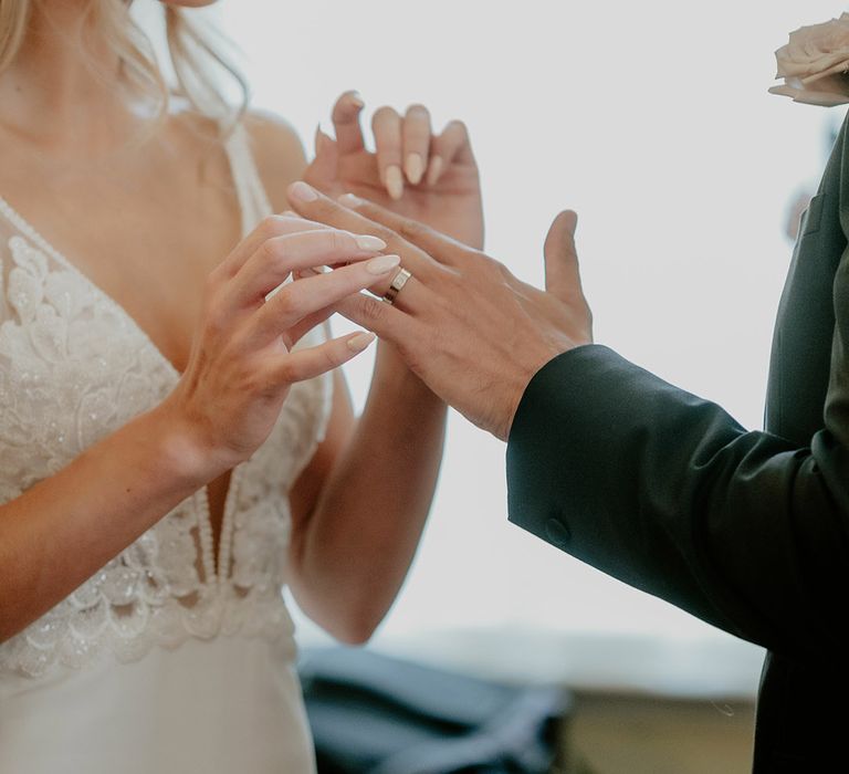 Bride smiles with nude painted almond wedding nails after putting on the groom's Cartier wedding ring 