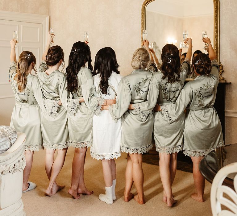 Bride wears white silk short dressing gown alongside her bridesmaids who wear matching dressing gowns in sage green