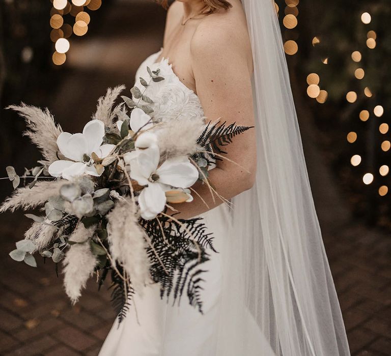 Bride in white strapless wedding dress with white flower and pampas grass bouquet 