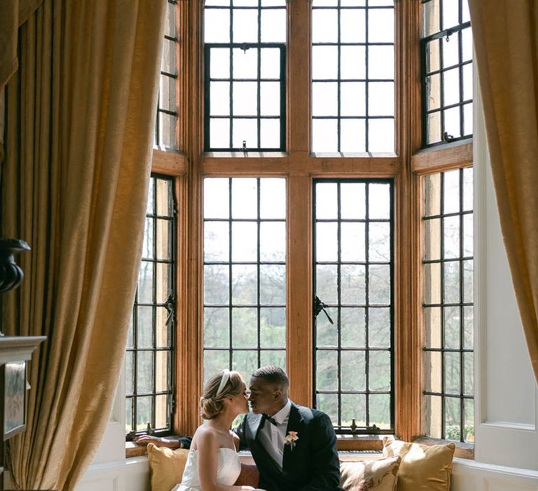 Bride and groom sit together at Ruston Hall and lean in for a kiss for their classic country house wedding 