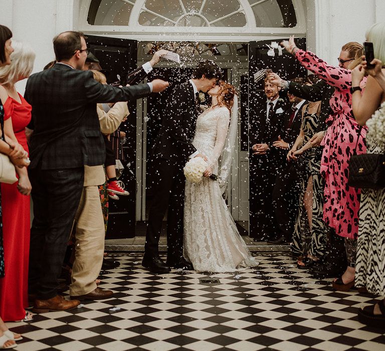 Bride wears lace wedding dress and kisses her groom outside the Belair House whilst confetti is thrown around them