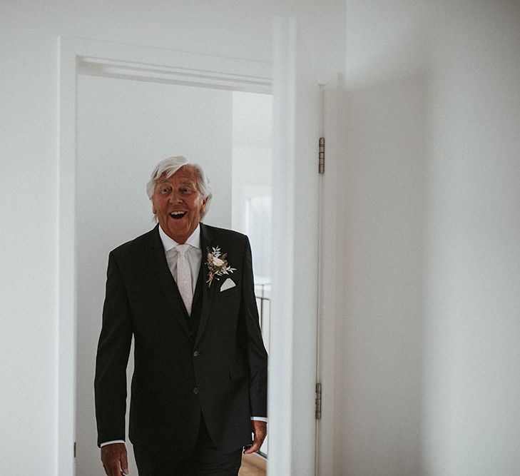 Bride's father wears three-piece black suit and floral buttonhole sees his daughter for the first time 